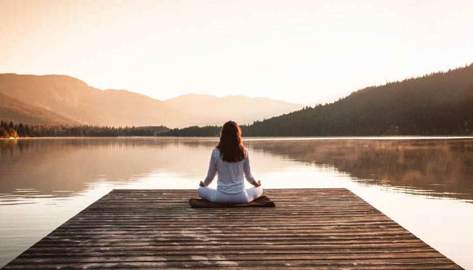 Frau im Lotussitz auf einem Steg am Wasser – ruhiger Moment während eines Retreats